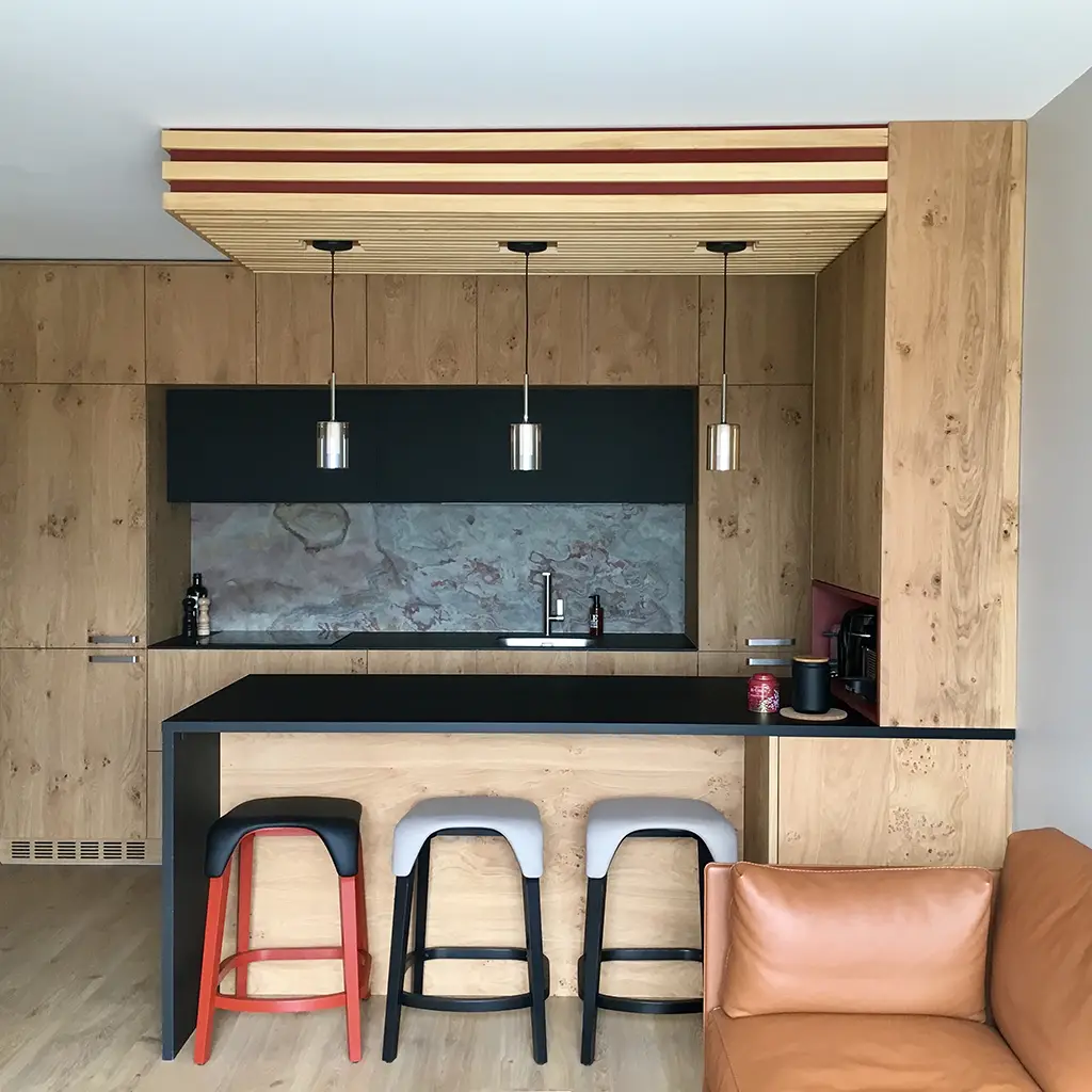 Cuisine ouverte moderne avec meubles en bois clair, plan de travail noir et luminaires suspendus design dans un appartement rénové par Home Feeling dans le Val d'Oise