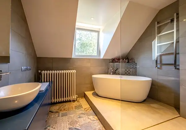 Salle de bain sous combles avec baignoire îlot, vasque ronde et carrelage effet pierre, design par Home Feeling à Montmorency