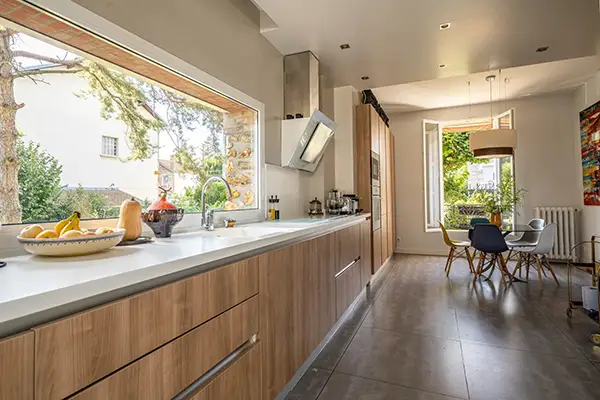 Cuisine linéaire baignée de lumière grâce à une grande baie vitrée installée par Home Feeling dans une meulière à Montmorency