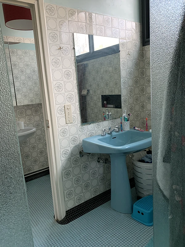 Ancienne salle d'eau des années 80 avec lavabo sur colonne bleu et carrelage vieillot avant travaux de rénovation par Home Feeling dans le Val d'Oise