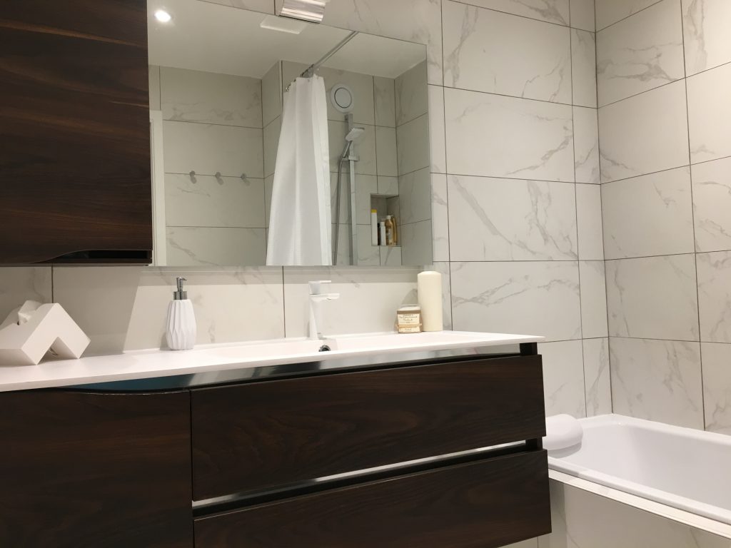 Salle de bain contemporaine avec meuble vasque suspendu en bois sombre et carrelage effet marbre blanc dans un appartement rénové par Home Feeling dans le Val d’Oise