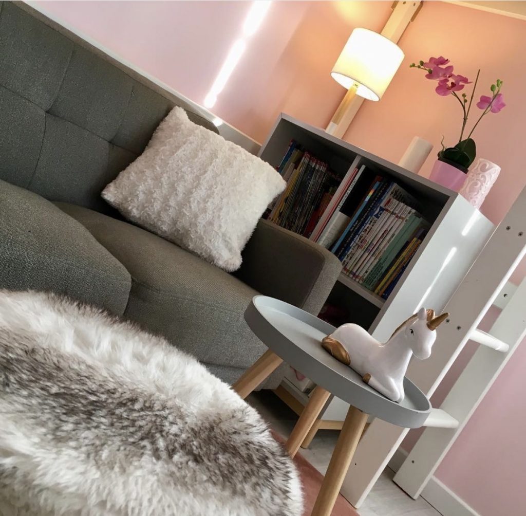 Espace détente pour enfant avec petit canapé gris, tapis en fourrure blanche et bibliothèque basse dans un appartement rénové par Home Feeling dans le Val d’Oise